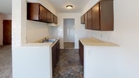 Located at 1032 S 23rd St. in Richmond, Indiana, this single-floor residence offers a well-organized layout across a variety of functional living spaces. The galley-style kitchen is equipped with rich dark brown cabinetry lining both walls, light-toned countertops, a built-in sink, and durable stone-look tile flooring. A pass-through peninsula connects the kitchen to the adjacent living area, creating an open, communicative flow between the two spaces. The living area is generously proportioned, featuring wall-to-wall carpeting, large windows that allow ample natural light, and a wall-mounted air conditioning unit for climate control. A half-wall divider with a built-in shelf adds architectural interest and helps define the transition between spaces. The bedrooms are carpeted throughout and share a clean, bright aesthetic with white walls and blinds-covered windows. Several bedrooms feature ceiling fans and baseboard heating, ensuring year-round comfort. One standout room showcases a full accent wall clad in rustic horizontal wood planking, providing a warm and characterful contrast to the otherwise neutral palette. The overall ambiance of the home is clean, functional, and move-in ready, with consistent finishes and a practical, well-connected floor plan throughout.