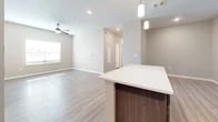 This well-appointed single-floor residence at 2101 Williamson Rd in Griffin, Georgia offers a thoughtfully designed layout with modern finishes throughout. The open-concept kitchen serves as the heart of the home, showcasing rich dark-toned cabinetry with brushed nickel hardware, crisp white countertops, a central island with pendant lighting overhead, and black appliances including a refrigerator, range, microwave, and dishwasher. Wood-look luxury vinyl plank flooring extends through the kitchen and living areas, while the living room provides a comfortable, open feel complemented by a ceiling fan and natural light from nearby windows. The bedrooms are carpeted and feature neutral warm tones, with windows that offer outdoor views of the surrounding landscape. Each bedroom includes closet space with built-in shelving for practical storage. The bathroom is finished with dark wood vanity cabinetry, a white countertop, a large mirror, a walk-in shower, and wood-look flooring that ties the space together cohesively. Throughout the home, clean white trim, panel-style doors, and a neutral color palette create a consistent, modern aesthetic that is both functional and inviting.
