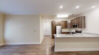 This single-floor residence is designed with a clean, functional layout that connects the main living areas seamlessly. The entryway opens into a spacious living area finished with warm wood-style flooring and neutral beige walls accented by crown molding. A glass-paneled door and adjacent window allow natural light to fill the room, creating a bright and welcoming atmosphere.

The kitchen is a standout feature, equipped with rich medium-toned cabinetry extending to the ceiling for generous storage. Light granite countertops provide ample prep space, and a peninsula with an integrated sink offers additional workspace while maintaining an open connection to the living area. Stainless steel appliances, including a refrigerator, range, and over-the-range microwave, complete the well-appointed kitchen.

The bedrooms are carpeted in neutral tones, offering a quieter, softer contrast to the hard flooring in the main areas. Each room is finished with the same consistent beige palette and white panel doors. The bathroom features wood-style flooring, a full-sized soaking tub with a shower rod, and a toilet, providing a practical and clean design. Recessed lighting and crown molding are consistent throughout, lending the space a cohesive and polished finish.