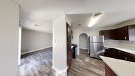 This single-floor residence offers a thoughtfully designed layout with consistent wood-look vinyl flooring and a neutral color palette throughout. The kitchen is a functional highlight, featuring rich dark-toned cabinetry, light quartz countertops, stainless steel appliances including a gas range, refrigerator, built-in microwave, and dishwasher, along with a double basin sink positioned beneath a window. A charming arched passageway connects the kitchen to the rest of the living areas, adding an architectural accent that carries through multiple rooms. The open living area is bright and generously proportioned, with a sliding glass door that leads to an outdoor patio, allowing for natural light and outdoor access. The bedrooms are well-sized, each featuring windows that bring in natural light, textured ceilings, and access to closet space. The bathroom includes a vessel sink atop a dark wood vanity, a wide mirror with overhead vanity lighting, and a full soaking tub. Textured ceilings are consistent throughout the home. The overall design balances practicality and clean aesthetics, creating a comfortable and move-in ready living environment.