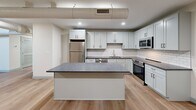 Located at 160 Seabury St in Fall River, MA, this two-bedroom, three-bathroom residence spans two floors and showcases a thoughtful blend of historic architectural character and modern finishes. One of the most distinctive features is the soaring arched ceiling visible from the upper level, lending a dramatic, church-like quality to the space and setting it apart from conventional layouts.

The main floor offers a generous footprint housing the kitchen, living areas, and stairwell. The kitchen is well-appointed with white shaker cabinetry, granite countertops, a subway tile backsplash, stainless steel appliances including a refrigerator, range, microwave, and dishwasher, and a central island ideal for dining or prep work. Light hardwood-style flooring runs throughout both levels, contributing to a warm, cohesive aesthetic.

A striking staircase with wood treads and a black metal railing connects the two floors, with wall sconces illuminating the upper landing beneath the arched ceiling. The upper level contains both bedrooms, each finished with light walls and hardwood-style flooring. The primary bedroom includes a closet and an en-suite bathroom. Additional bedrooms and bathrooms are well-sized and cleanly finished. The bathrooms feature gray shaker vanities with granite countertops and neutral tile flooring. In-unit laundry with a front-loading washer and dryer is also included.