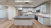 Located at 160 Seabury St in Fall River, MA, this two-bedroom, three-bathroom residence spans two floors and showcases a thoughtful blend of historic architectural character and modern finishes. One of the most distinctive features is the soaring arched ceiling visible from the upper level, lending a dramatic, church-like quality to the space and setting it apart from conventional layouts.

The main floor offers a generous footprint housing the kitchen, living areas, and stairwell. The kitchen is well-appointed with white shaker cabinetry, granite countertops, a subway tile backsplash, stainless steel appliances including a refrigerator, range, microwave, and dishwasher, and a central island ideal for dining or prep work. Light hardwood-style flooring runs throughout both levels, contributing to a warm, cohesive aesthetic.

A striking staircase with wood treads and a black metal railing connects the two floors, with wall sconces illuminating the upper landing beneath the arched ceiling. The upper level contains both bedrooms, each finished with light walls and hardwood-style flooring. The primary bedroom includes a closet and an en-suite bathroom. Additional bedrooms and bathrooms are well-sized and cleanly finished. The bathrooms feature gray shaker vanities with granite countertops and neutral tile flooring. In-unit laundry with a front-loading washer and dryer is also included.