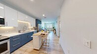 Located at 164 Lexington Rd in Billerica, MA, this modern one-bedroom, one-bathroom residence offers a well-organized single-floor layout with clean contemporary finishes throughout. The open-concept kitchen is a standout feature, showcasing bold navy lower cabinets contrasted by crisp white upper cabinetry, under-cabinet lighting, a white subway tile backsplash, stainless steel appliances, and light wood-style flooring that flows seamlessly into the living area. A movable kitchen island with a butcher block top adds flexible dining and prep space. The living room is bright and welcoming, with a large window inviting natural light and views of the surrounding neighborhood. The bedroom offers a calm retreat with plush carpeting, a generous window with outdoor views, and access to two closets, providing ample storage. The bathroom features a sleek gray vanity with a white countertop, wood-look tile flooring, and a clean, minimalist aesthetic. Additional practical spaces include a dedicated laundry area, a utility room, and a hallway connecting the layout efficiently. Throughout, the neutral palette, recessed lighting, and modern hardware create a cohesive, polished atmosphere well-suited for everyday living.