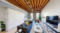 Located at 1350 North Wells Street in Chicago's vibrant Old Town neighborhood, this single-floor loft masterfully combines industrial heritage with contemporary living. Exposed brick walls and richly textured timber beam ceilings with visible wooden joists define the architectural character throughout, while light hardwood flooring and clean white walls provide a modern contrast.

The open-plan main area seamlessly integrates the living room, dining space, and kitchen. The living zone features ample room for seating and entertainment, with natural light streaming through large windows that frame city views. The kitchen is outfitted with sleek gray cabinetry, stainless steel appliances including a gas range and full-size refrigerator, a white tile backsplash, and a marble-topped island with bar seating — ideal for dining and casual gatherings. Track lighting and an exposed HVAC duct add to the industrial aesthetic overhead.

The sleeping area is tucked within the open layout, anchored by an exposed brick wall and a generous window with views of the Chicago skyline. A full bathroom features a tub-shower combination, vanity with storage, and neutral tile flooring. Additional conveniences include a dedicated closet, a hallway, a laundry area, and a utility room, ensuring practical functionality throughout this well-appointed urban loft.
