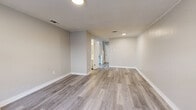 Located at 420 Lake Hill Dr in Vicksburg, Mississippi, this two-story home offers two bedrooms and two bathrooms across a well-organized layout. The ground floor houses the main living areas, including an open-concept dining and living room finished with light gray luxury vinyl plank flooring and neutral-toned walls that create a bright, clean atmosphere. The kitchen is efficiently designed with white cabinetry, a white countertop with an undermount sink, and black appliances including a full-size refrigerator and electric range with overhead ventilation. A window above the sink allows natural light to filter in. The upper floor contains both bedrooms, each with the same cohesive gray LVP flooring and soft neutral walls. The primary bedroom is generously sized and features dual closets, crown molding, and access to a hallway. A second bedroom includes a notable shiplap-style accent wall and a window with natural light. Each floor is served by its own bathroom, one of which includes a full tub-shower combination with brushed nickel fixtures. Two staircases and a hallway connect the floors, adding to the functional flow of the home. Throughout, the space maintains a clean, updated aesthetic with consistent finishes.