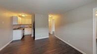 This single-floor unit offers a straightforward and functional layout designed for comfortable everyday living. Dark hardwood-style flooring runs throughout the space, providing a cohesive and modern look that contrasts cleanly with the light gray walls and bright white baseboards.

The living area is open and well-proportioned, with a textured ceiling and a front entry door that includes a sidelight window, allowing natural light to filter in. The space connects seamlessly to the kitchen, which is equipped with white cabinetry, granite-style countertops, a double-basin stainless steel sink, a gas range, and a full-size black refrigerator. A closet adjacent to the kitchen adds convenient storage.

The bedroom is a quiet, private space featuring a ceiling fan with integrated lighting and a window fitted with white blinds that provides natural light and ventilation. The neutral wall tones and consistent flooring keep the room feeling cohesive with the rest of the unit.

The bathroom is efficiently designed, featuring a stand-alone walk-in shower with a chrome showerhead and curtain rod, a toilet, and a granite-style vanity surface. The soft gray walls and clean white fixtures give the bathroom a simple, tidy aesthetic. Overall, the unit presents a clean, move-in-ready environment with updated finishes throughout.