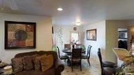This single-floor residence offers a welcoming and well-appointed interior designed for comfortable everyday living. The open layout seamlessly connects the living and dining areas, creating a cohesive and functional space. The living area features a plush brown leather sofa adorned with decorative throw pillows, complemented by framed wall art that adds a warm, homey character to the room. Recessed ceiling lighting provides a clean, modern touch overhead.

The dining area is furnished with a round dark-wood table surrounded by matching upholstered chairs, making it an ideal setting for intimate meals. Decorative elements such as tall vases with dried branches and wall-mounted botanical accents lend a natural, organic aesthetic to the space. A window in the dining area allows natural light to filter in, brightening the room.

The flooring throughout features a distinctive patterned tile design that ties the two areas together visually while adding a layer of texture and interest underfoot. Neutral-toned walls serve as a clean backdrop, allowing the furnishings and décor to take center stage. Overall, the space exudes a cozy, lived-in warmth that is both functional and aesthetically pleasing.