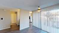Located at 3950 Leland in San Diego, Unit D20 is a single-floor residence thoughtfully designed with updated interiors and a practical layout. The open living area is anchored by rich, dark hardwood-style flooring and features a ceiling fan, a wall-mounted intercom panel, and a large sliding glass door fitted with vertical blinds that allows generous natural light to fill the space and provides access to an outdoor area with greenery views.

The kitchen is well-appointed with white shaker-style cabinetry extending to ceiling height, gray countertops, and a full suite of stainless steel appliances including a refrigerator, electric range, and over-the-range microwave. A breakfast bar separates the kitchen from the living space, enhancing the open flow.

The bedrooms feature plush carpeting and large windows dressed with horizontal blinds, inviting ample natural light. The primary bedroom includes access to a dedicated bathroom with white vanity cabinetry and a glass-enclosed shower, as well as a spacious walk-in closet. A secondary bathroom offers a full soaking tub with a shower. Throughout, the unit maintains a clean, neutral palette with white trim and warm-toned walls.