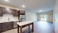 Located at 240 Thompson Ave E in West St. Paul, Minnesota, this thoughtfully designed one-bedroom, one-bathroom residence offers a functional and modern living experience across a single floor. The open-concept kitchen and living room serve as the heart of the home, featuring rich dark-stained cabinetry, white subway tile backsplash, stainless steel appliances including a refrigerator, dishwasher, range, and microwave, and light-toned wood-style flooring that extends throughout the main living area. A sliding glass door in the living room opens to a private balcony with views of mature trees, filling the space with natural light and greenery. The bedroom is generously sized, finished with plush carpeting, a large window overlooking the outdoors, and access to a spacious walk-in closet equipped with wire shelving systems for ample storage. The bathroom features dark wood cabinetry, a white countertop vanity, a large mirror, and light wood-style tile flooring. A stacked washer and dryer unit is conveniently located within the bathroom, adding in-unit laundry functionality. Additional storage is provided by two closets, along with a dedicated utility room. The neutral color palette and clean finishes throughout create a bright, cohesive ambiance well-suited for comfortable everyday living.