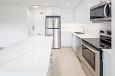 Located on the ninth floor at 30 Edith Street in Toronto's midtown neighbourhood, Unit 903 is a well-appointed suite that combines contemporary design with a clean, minimal aesthetic throughout. Light hardwood flooring flows seamlessly across the entire unit, complementing the crisp white walls and creating a bright, airy atmosphere.

The open-concept kitchen serves as a central feature of the living space, equipped with high-gloss white cabinetry extending to the ceiling, stainless steel appliances including a refrigerator, electric range, over-the-range microwave, and dishwasher. A large kitchen island with a light stone countertop provides additional workspace and casual seating, while recessed pot lighting overhead adds a polished finish.

The living area is spacious and filled with natural light from floor-to-ceiling windows fitted with roller shades, offering treetop views of the surrounding Toronto landscape. Baseboard heating runs along the window walls throughout the unit. The bedrooms are generously sized, each featuring windows with outdoor views and roller shades for privacy. One bedroom includes a dedicated closet with built-in shelving and hanging rails. An en-suite or adjacent bathroom is accessible from the bedroom area. A hallway connects the private sleeping quarters to the main living space, completing the functional and well-organized layout of this modern suite.