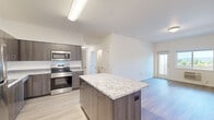This single-floor unit offers four bedrooms and two bathrooms within a efficiently designed layout. The open-concept kitchen and living area serves as the central hub of the space, where a standout granite-topped island with dark wood cabinetry provides both additional prep space and a casual gathering area. The kitchen is well-appointed with a full suite of stainless steel appliances, including a range, microwave, dishwasher, and refrigerator, complemented by matching dark wood cabinetry that extends to the ceiling for ample storage. Light wood-style flooring runs consistently throughout the unit, contributing to a clean, cohesive aesthetic.

The living area is open and functional, with a door and window that introduce natural light and outdoor views. The four bedrooms are modestly sized, featuring neutral white walls, the same light flooring, and vaulted ceilings in select rooms. A dedicated closet with wire shelving provides organized storage. The two bathrooms mirror the kitchen's design language, featuring granite countertops, dark wood vanities, and a tub-shower combination. The overall ambiance is modern, clean, and neutral throughout.