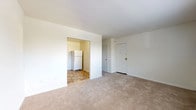 This single-floor unit at 8723 West Chester Pike in Upper Darby, PA offers a straightforward, functional layout across several well-defined spaces. The living area is bright and open, featuring neutral wall-to-wall carpeting, crisp white walls, and a window that allows natural light to fill the room. A wall-mounted air conditioning unit and baseboard heating provide year-round climate control. The space flows directly into a dedicated kitchen area, which is finished with warm oak cabinetry, dark laminate countertops, a stainless steel sink, and white appliances including a refrigerator, electric range, and dishwasher. Durable stone-patterned tile flooring runs throughout the kitchen. A secondary carpeted room — suitable as a bedroom — mirrors the living area in its clean, minimal design, also featuring a window with an outdoor view and baseboard heating. The full bathroom is efficiently appointed with white tile wainscoting, a vanity with under-sink storage, a medicine cabinet mirror, and matching stone-patterned tile flooring consistent with the kitchen. The overall aesthetic throughout the unit is clean and neutral, offering a move-in ready space with practical amenities in a convenient Upper Darby location.