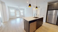 This single-floor residence showcases a contemporary design with clean lines and a neutral palette throughout. The open-concept kitchen and living area serves as the heart of the home, anchored by a large central island with a white quartz countertop, an undermount sink, and a stainless steel dishwasher beneath. Two sleek pendant lights hang above the island, adding warmth to the space. Dark wood-grain cabinetry lines the kitchen walls, complemented by stainless steel appliances including a refrigerator, range, and microwave. Light wood-tone flooring extends through the kitchen and living area, which is bright and airy thanks to multiple windows fitted with horizontal blinds. A ceiling fan adds to the comfort of the living space.

The bedrooms feature plush carpeting, generous windows for natural light, and walk-in closets with built-in shelving. The bathrooms are finished with dark wood-grain vanities, white quartz countertops, undermount sinks, and tub-shower combinations. One bathroom features a well-lit vanity mirror, while both maintain a clean, minimalist aesthetic consistent with the rest of the home. The overall ambiance is modern, bright, and move-in ready.