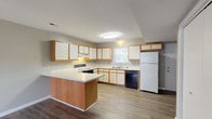 This two-story townhome features two bedrooms and two and a half bathrooms across a well-organized floor plan. The main level opens into a spacious living area finished with wood-look laminate flooring and a ceiling fan overhead. The open layout flows directly into the kitchen, which is equipped with white cabinetry trimmed in warm wood tones, light countertops, a peninsula with additional storage, and a full suite of appliances including an electric range, dishwasher, and refrigerator. A window above the sink allows natural light into the kitchen. A half bathroom on the main level features a corner-mount sink, wood-look flooring, and neutral gray walls, offering convenience for guests. The upper level houses both bedrooms, each featuring plush carpeting, ceiling fans, and windows that bring in natural light. The full bathrooms on this level include wood-look flooring, a tub-shower combination, and a vanity with a sink. Neutral gray walls throughout the townhome create a cohesive and understated aesthetic, while the mix of laminate and carpet flooring distinguishes the living spaces across both floors.