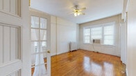 This well-appointed 1-bedroom, 1-bathroom residence showcases a blend of classic character and practical design throughout its single-floor layout. Rich, warm-toned hardwood floors run continuously through the main living areas, reflecting natural light and adding a timeless quality to the space.

The living room is generously sized, featuring a ceiling fan with light fixture, a traditional cast-iron radiator, and a French door with glass panes that adds an elegant architectural touch. Multiple windows fitted with blinds allow for ample natural light and include a window air conditioning unit for climate control.

The bedroom offers a comfortable layout with built-in shelving along one wall, large triple windows that flood the room with light, and the same gleaming hardwood floors. A wall-mounted sconce provides warm accent lighting.

The kitchen is efficiently designed with white cabinetry, dark granite-style countertops, a mosaic tile backsplash in neutral tones, a gas range, and a full-size refrigerator — all set on hardwood flooring.

The bathroom retains its vintage charm with terracotta tile flooring, white subway-style wall tiles, a classic pedestal sink, and a wall-mounted vanity mirror with sconce lighting. A window provides natural ventilation. Overall, the space exudes a charming, classic character throughout.