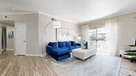 This thoughtfully designed 3-bedroom, 2-bathroom single-floor residence offers a comfortable and functional layout across a well-utilized footprint. The open-concept living area is a standout feature, finished with wood-look luxury vinyl flooring, crown molding, and neutral warm-toned walls that create a bright and welcoming ambiance. A sliding glass door floods the space with natural light and provides direct access to a private balcony with outdoor views. The adjoining dining area features the same flooring and is complemented by an oval mirror accent wall detail. The kitchen is galley-style with warm wood cabinetry, dark countertops, white appliances, and convenient access to an in-unit laundry room. The three bedrooms are carpeted and generously proportioned, with the primary bedroom offering ample space for a full furniture arrangement. The two bathrooms are finished with wood-look tile flooring, warm wood vanities, large mirrors with bar lighting, and shower-tub combinations. Throughout the home, a cohesive neutral palette, consistent flooring materials, and well-placed windows contribute to a bright, calm, and livable atmosphere well-suited for everyday comfort.