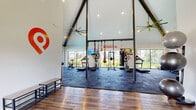 Located at 3535 SW 20th St in Ocala, FL, this single-story fitness center is designed to inspire and motivate with its striking architectural details and thoughtfully curated equipment layout. The space is defined by dramatic vaulted ceilings with exposed dark beams, creating an open, airy atmosphere that feels expansive and energizing. Large floor-to-ceiling windows line the walls, flooding the interior with natural light and offering views of the surrounding green landscape and resort-style pool area beyond.

The main workout floor is finished with durable rubber sport tiles, providing a safe and functional surface for a wide variety of exercises. The cardio zone features treadmills, elliptical machines, and a rowing machine, while the strength training area is equipped with a full dumbbell rack, a power rack with weight plates, and suspension training systems. A dedicated heavy bag and functional training rig add versatility for combat and cross-training workouts.

The entryway features warm hardwood-style flooring and opens seamlessly into the main gym floor, offering a welcoming transition into the workout space. Motivational wall graphics reinforce the fitness-focused atmosphere throughout. Large ceiling fans ensure comfortable airflow, and recessed lighting supplements the abundant natural light. The space offers a complete and well-rounded fitness experience in a bright, modern facility.