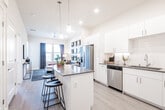 This well-appointed single-floor residence showcases a thoughtfully designed open-concept layout that seamlessly connects the kitchen, dining, and living areas. The kitchen is a standout feature, boasting crisp white cabinetry, dark quartz countertops, a generous center island with bar seating, and a full suite of stainless steel appliances including a refrigerator, range, microwave, and dishwasher. Pendant lighting and recessed fixtures illuminate the space, while light wood-tone flooring runs throughout, adding warmth and continuity.

The living room offers a bright and inviting retreat, featuring a ceiling fan, large windows dressed with navy drapes that frame outdoor views, and ample wall space accented with decorative mirrors — creating a stylish, comfortable atmosphere.

Two well-sized bedrooms provide restful sanctuaries, each with plush carpeting, large windows that welcome natural light and outdoor scenery, and generous closet space. The bathroom is clean and functional, featuring a full tub-shower combo and wood-tone flooring that ties in with the rest of the home.

Overall, the residence exudes a modern, contemporary aesthetic with neutral tones, quality finishes, and an efficient, open floor plan that maximizes both comfort and functionality.