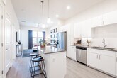 This well-appointed single-floor residence showcases a thoughtfully designed open-concept layout that seamlessly connects the kitchen, dining, and living areas. The kitchen is a standout feature, boasting crisp white cabinetry, dark quartz countertops, a generous center island with bar seating, and a full suite of stainless steel appliances including a refrigerator, range, microwave, and dishwasher. Pendant lighting and recessed fixtures illuminate the space, while light wood-tone flooring runs throughout, adding warmth and continuity.

The living room offers a bright and inviting retreat, featuring a ceiling fan, large windows dressed with navy drapes that frame outdoor views, and ample wall space accented with decorative mirrors — creating a stylish, comfortable atmosphere.

Two well-sized bedrooms provide restful sanctuaries, each with plush carpeting, large windows that welcome natural light and outdoor scenery, and generous closet space. The bathroom is clean and functional, featuring a full tub-shower combo and wood-tone flooring that ties in with the rest of the home.

Overall, the residence exudes a modern, contemporary aesthetic with neutral tones, quality finishes, and an efficient, open floor plan that maximizes both comfort and functionality.
