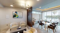 Located along the scenic Boardwalk Trail in Austin, TX, this co-working space delivers a polished, amenity-rich environment designed to accommodate both focused work and collaborative interaction. The single-floor layout is thoughtfully organized into distinct functional zones, separated by a striking slatted wood partition that adds architectural warmth while maintaining an open, airy feel throughout.

The lounge area features plush cream-toned armchairs, a low-profile coffee table, and a bold abstract artwork, anchored by a mid-century-inspired brass and glass chandelier overhead. Adjacent to this seating zone, a dedicated workstation area provides computer terminals, a printer, and ergonomic seating, accessible through a glass-etched entry marked "Co-Work."

A banquette seating section offers a channel-tufted upholstered bench paired with round tulip-style tables, ideal for informal meetings or individual work. The space transitions into a brighter lounge area crowned by a coffered ceiling with warm ambient LED lighting, where floor-to-ceiling windows frame sweeping views of the adjacent waterway and lush tree canopy. Natural light fills this zone generously, complemented by sheer drapery and a refined mix of contemporary furnishings that complete the sophisticated, welcoming atmosphere.