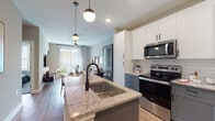 This well-appointed single-floor residence offers a thoughtfully designed open-concept layout that seamlessly connects the kitchen, dining, and living areas. The kitchen is a standout feature, showcasing granite countertops, a large central island with an undermount sink and pendant lighting, two-tone cabinetry with white upper cabinets and slate-gray lower cabinets, a classic subway tile backsplash, and a full suite of stainless steel appliances including a refrigerator, electric range, and over-the-range microwave. Light wood-style flooring flows consistently throughout the space, enhancing the sense of openness and continuity. The living area is bright and inviting, benefiting from generous natural light streaming through large sliding glass doors that lead to an outdoor area, complemented by a ceiling fan overhead. Neutral wall tones and contemporary finishes create a calm, modern ambiance throughout. The bathroom continues the design language of the home, featuring granite countertops, white cabinetry with matte black hardware, a large vanity mirror, and wood-style flooring. A spacious walk-in closet with built-in shelving and hanging storage is accessible directly from the bathroom, providing ample organization. Overall, this residence combines clean, modern aesthetics with functional design details.