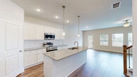 Located at 352 Stately Oaks Court in Hoschton, GA, this well-appointed two-story home offers four bedrooms, three bathrooms, and a thoughtfully designed layout across two floors. The main level features an open-concept kitchen and living area bathed in natural light from large windows and a rear glass door leading to an outdoor space. The kitchen is a standout, showcasing granite countertops, a central island with a built-in sink, white shaker cabinetry, stainless steel appliances including a double oven and side-by-side refrigerator, and elegant pendant lighting. The living room extends naturally from the kitchen, with warm hardwood-style flooring and a ceiling fan overhead. Upstairs, the spacious primary bedroom is accompanied by an en-suite bathroom featuring a glass-enclosed walk-in shower, granite vanity, and white cabinetry. A generous walk-in closet with wire shelving offers ample storage. Three additional bedrooms provide flexibility for guests or home office use. A dedicated laundry room with full-size washer and dryer hookups adds convenience. Consistent hardwood-style flooring, neutral tones, recessed lighting, and clean white trim unify the home's modern aesthetic throughout both levels.