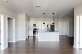 This single-floor unit showcases a thoughtfully designed open-concept layout that seamlessly connects the kitchen, dining, and living areas. The kitchen serves as the centerpiece, featuring a large island with granite countertops, an undermount sink with a matte black faucet, and white shaker cabinetry accented by black hardware. A white subway tile backsplash complements the stainless steel appliance suite, which includes a range, over-the-range microwave, dishwasher, and refrigerator. Industrial-style pendant lights hang above the island, adding a contemporary touch.

Dark hardwood flooring flows throughout the main living areas, contrasting elegantly with the crisp white walls. The living area benefits from natural light through large windows and sliding door access to an outdoor balcony, with a ceiling fan overhead. The bedrooms offer a calm retreat; one features plush carpet and a ceiling fan, while another provides hardwood-style flooring and a window view. The bathroom is well-appointed with a subway tile tub surround, granite vanity, white cabinetry, and an adjacent walk-in closet. Throughout the space, a neutral, modern palette creates a clean and cohesive ambiance.