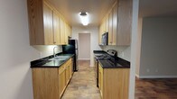 This single-floor residence offers a well-organized layout with distinct functional zones connected by consistent hardwood-style flooring throughout. The galley-style kitchen is a standout feature, lined on both sides with light oak cabinetry that extends to the ceiling, providing generous storage. Dark granite countertops contrast cleanly against the cabinetry, while a black tile backsplash adds a sharp, defined accent. The kitchen is equipped with stainless steel appliances, including a refrigerator, microwave, and electric range, along with a double-basin sink beneath overhead cabinetry. Flush ceiling lighting keeps the space well-illuminated.

The open living area is spacious and versatile, with neutral-toned walls and rich, dark hardwood-style flooring that lends warmth to the room. A ceiling fan provides air circulation, and a baseboard heater is present along the wall. A sliding glass door fills the living space with natural light and provides direct access to an outdoor area with visible greenery, enhancing the overall ambiance.

The bathroom is clean and functional, featuring a white vanity with under-sink storage, a large mirror with a lighted bar above, and a glass-enclosed shower, all set against a neutral color palette that keeps the space feeling bright and airy.