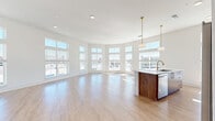 Located at 2124 American Industrial Way in Chamblee, GA, this well-appointed two-bedroom, two-bathroom residence offers a thoughtfully designed single-floor layout with generous living space. The open-concept living and kitchen area is a standout feature, highlighted by a dramatic curved wall of large, multi-pane windows that flood the room with natural light and provide sweeping outdoor views. Light-toned hardwood flooring runs throughout the main living areas, enhancing the bright, airy atmosphere.

The kitchen is both functional and stylish, featuring a central island with a white quartz countertop and an undermount sink with a gold-tone faucet, rich wood cabinetry with brass hardware, white upper cabinets, a geometric tile backsplash, and stainless steel appliances including a range, microwave, and refrigerator. Pendant lighting with gold accents adds a modern finishing touch.

Both bedrooms are carpeted and well-lit by large windows with outdoor views. The spacious primary bedroom includes a walk-in closet with built-in wire shelving. The bathrooms feature clean white cabinetry, white countertops, and wood-framed mirrors, complemented by hardwood-style flooring. The overall aesthetic is modern and light-filled, with a neutral palette throughout.