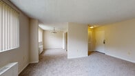 This single-floor residence offers a practical and comfortable layout designed to maximize livable space. The open living area is generously sized, featuring neutral-toned carpet, soft cream-colored walls, and a textured ceiling that adds a classic touch. A large window fitted with vertical blinds allows natural light to fill the room, while a baseboard radiator ensures year-round comfort. A pendant light fixture accentuates the transition toward the hallway, which connects the main living space to the rest of the unit.

The kitchen is equipped with warm maple cabinetry offering ample storage, granite-look countertops, and a stainless steel gas range with a built-in overhead ventilation hood. Light hardwood-style flooring grounds the kitchen's practical design. A dishwasher is also present, adding to the room's functionality.

The bedrooms are carpeted and well-proportioned, with neutral walls that provide a clean, versatile backdrop. One bedroom features a louvered closet door, providing convenient built-in storage. The bathroom includes a full tub-shower combination with tiled surround, light tile flooring, and a ventilation fan overhead. The dedicated entryway provides a clear transition into the home, completing this thoughtfully arranged floor plan.