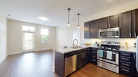 This single-floor residence offers a thoughtfully designed open-concept layout that seamlessly connects the kitchen and living area. The kitchen is a standout feature, showcasing rich dark espresso cabinetry, granite countertops, a central island with a double sink, stainless steel appliances including a refrigerator, range, microwave, and dishwasher, and elegant pendant lighting that adds a modern touch. Wood-style flooring runs throughout the main living area, enhancing the warm and inviting ambiance.

The living space is bright and airy, benefiting from multiple windows fitted with blinds that allow for natural light and outdoor greenery views. Each bedroom is carpeted for comfort, equipped with a ceiling fan, and features windows that frame pleasant outdoor scenery.

The primary bathroom is finished with matching granite countertops, dark cabinetry, tile flooring, and leads directly into a spacious walk-in closet outfitted with wire shelving systems for organized storage. A secondary bathroom mirrors the same refined design aesthetic with a granite vanity top and large mirror. Overall, the space presents a cohesive, contemporary style with quality finishes throughout.