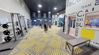 Located at 1206 NW Tahoe Ln in Silverdale, Washington, this single-floor fitness facility is designed to provide a comprehensive and energizing workout environment. The main exercise floor is expansive and open, featuring bold, geometric yellow-and-gray patterned carpet tiles that create a dynamic and motivating visual atmosphere. Recessed lighting is mounted on a deep navy ceiling, ensuring the space is well-lit throughout.

The strength training area is equipped with a variety of cable machines and resistance equipment, arranged to allow easy circulation between stations. Motivational banners and fitness imagery are displayed along the deep blue accent walls, reinforcing the facility's active and goal-oriented culture. Wall-mounted televisions provide entertainment and information throughout the workout area.

Typography-styled signage on a prominent white column highlights the facility's core offerings — including Training, Body, Endurance, Aerobics, and more — guiding members through the available zones. A doorway leads to an adjoining room, suggesting additional dedicated spaces for classes or specialized training. Functional accessories such as stability balls and resistance tools are visible throughout, rounding out the facility's well-equipped and purpose-driven design.