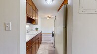Located at 1266 Gorman Ave in West St. Paul, MN, this one-bedroom, one-bathroom unit offers a practical and comfortable single-floor layout. The galley-style kitchen is well-appointed with warm wood cabinetry lining both sides, light countertops with marble-style detailing, a white electric range with overhead ventilation, a full-size refrigerator, and a utility sink — providing ample storage and functionality. The kitchen flows openly into the combined living area, which features light-toned laminate wood flooring, a ceiling fan, and neutral white walls that create a bright, airy atmosphere. The living area benefits from large windows framed in rich wood trim, offering pleasant views of surrounding greenery. The generously sized bedroom is carpeted for comfort and includes a built-in closet with louvered bi-fold doors, offering practical storage space. A baseboard heating system is present throughout. The full bathroom features a wood-framed vanity with an integrated sink, a large mirror with overhead lighting, classic white tile walls, mosaic tile flooring, and a shower-tub combination. This well-maintained unit provides a cozy, functional living environment in a quiet West St. Paul neighborhood.
