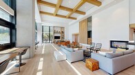 Located at 5075 Camino de la Siesta in San Diego, CA, this thoughtfully designed single-floor amenity space offers a seamless blend of comfort and functionality. The layout encompasses two generous living areas, two private offices, glass-enclosed meeting rooms, and additional flexible space, all unified by wide-plank light hardwood flooring that flows throughout.

The main living area commands attention with its soaring ceilings accented by warm wood beam detailing and a striking floor-to-ceiling glass wall that floods the interior with natural light and frames lush outdoor greenery. A sleek modern fireplace serves as a focal point, flanked by vibrant upholstered seating in bold hues. An adjacent lounge zone features built-in wood shelving, a wall-mounted display, and curated décor, creating a refined yet inviting atmosphere.

The lobby area includes a mailroom, a café-style bar counter with seating, and additional lounge furniture arranged for both casual conversation and quiet relaxation. Glass-partitioned private offices and meeting rooms offer transparency while maintaining acoustic separation, with the conference room benefiting from large windows overlooking the surrounding landscape.

Throughout the space, the interplay of white walls, natural wood elements, patterned tile accents, and abundant sunlight creates a bright, contemporary ambiance well-suited for community and professional use.