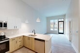 Located at 2111 Packard St in Ann Arbor, MI, this modern one-bedroom, one-bathroom unit offers a thoughtfully designed open-concept layout across a single floor. Soaring ceilings throughout create an airy, expansive feel well beyond the unit's compact footprint.

The combined living and dining area flows seamlessly into the kitchen, which features a peninsula with a white quartz countertop, undermount sink with a matte black faucet, light wood cabinetry, white upper cabinets with black hardware, and stainless steel appliances including a refrigerator, range, microwave, and dishwasher. Pendant lighting adds a contemporary touch. Light wood-tone luxury vinyl plank flooring runs throughout the main living areas.

Large windows in the living area invite abundant natural light and offer views of the surrounding Ann Arbor neighborhood. The bedroom is carpeted for comfort and includes a walk-in closet with wire shelving, as well as an additional closet. A second window in the bedroom provides further natural light and neighborhood views.

The bathroom is well-appointed with a glass-enclosed shower, white subway-style tile surround, white vanity with quartz countertop, matte black fixtures, and a large mirror with modern lighting. A dedicated laundry area and utility room add practical convenience to this well-rounded unit.