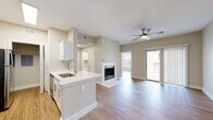 This single-floor residence offers a thoughtfully designed open-concept layout that seamlessly connects the main living spaces. The living room serves as the centerpiece of the home, featuring a classic fireplace with a clean white surround, a ceiling fan with built-in lighting, and sliding glass doors that lead to a private balcony, filling the space with abundant natural light. Warm hardwood-style flooring flows consistently throughout the entire unit, adding a cohesive and inviting aesthetic.

The kitchen is outfitted with white cabinetry, light quartz countertops, a peninsula with an integrated sink, and stainless steel appliances including a refrigerator and range. A dedicated entryway provides a welcoming transition into the living areas, complete with a security panel and convenient pass-through shelf.

The bedroom is generously proportioned, featuring its own ceiling fan, a large window with natural light, and a closet with sliding panel doors. The adjoining bathroom is well-appointed with white cabinetry, quartz countertops, a framed mirror, and a full soaking tub. Throughout the residence, neutral warm-gray wall tones and crisp white trim create a clean, modern ambiance that is both functional and comfortable.