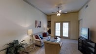 This well-appointed 2-bedroom, 2-bathroom single-floor residence offers a thoughtfully designed layout with comfortable and functional living spaces. The living room is a standout feature, boasting soaring vaulted ceilings that lend an open, airy feel to the space. A ceiling fan with integrated lighting is centrally positioned, providing both comfort and illumination. Built-in shelving in the corner offers practical display and storage options, while plush carpeting underfoot adds warmth throughout. Natural light pours into the living area through a set of elegant French doors fitted with plantation-style shutters, creating a bright and inviting atmosphere. The room comfortably accommodates a full seating arrangement, centered around a glass-top coffee table, making it ideal for both relaxing and entertaining. The neutral, warm-toned walls complement the traditional furnishings and décor, contributing to a cohesive and welcoming ambiance. With two full bedrooms and two bathrooms, this residence provides ample space for comfortable everyday living. The single-floor layout ensures easy accessibility and seamless flow between rooms, making this a practical and stylish home.