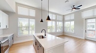 Located at 2307 North Tryon Street in Charlotte, NC, this well-appointed 2-bedroom, 2-bathroom unit offers a thoughtfully designed open-concept layout finished with warm hardwood-style flooring throughout. The combined kitchen and living area serves as the heart of the home, anchored by a large white quartz island with an integrated sink and pendant lighting overhead. The kitchen features white upper cabinetry, gray lower cabinets, a subway tile backsplash, and a full suite of stainless steel appliances. Soaring ceilings and floor-to-ceiling windows in the living area flood the space with natural light and provide direct access to a private balcony overlooking a landscaped courtyard. Both bedrooms are generously proportioned, each equipped with a ceiling fan and windows that invite ample daylight. The primary bathroom offers a glass-enclosed walk-in shower with white tile surround and dark matte fixtures, complemented by a gray vanity. The second bathroom includes a tiled shower-tub combo with matte black hardware. Two dedicated closets provide practical storage throughout. The unit's clean, contemporary aesthetic is carried consistently across every room, creating a cohesive and functional living environment.
