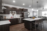 This single-floor residence at 11968 W Fairview Ave in Boise, Idaho, presents a thoughtfully designed open-concept layout that seamlessly connects the kitchen, dining, and living areas. The kitchen is a standout feature, outfitted with rich dark wood cabinetry, light quartz countertops, stainless steel appliances including a refrigerator, range, and dishwasher, and a generous island with pendant lighting overhead. A sliding barn door adds a modern architectural accent to the space. Wood-style flooring runs throughout the main living areas, lending warmth and continuity.

The living room is bright and welcoming, with natural light filtering through horizontal-blind-fitted windows and a ceiling fan overhead. The open floor plan allows for comfortable furniture arrangements and a clear flow between spaces.

The bedroom features plush carpeting, a window that invites natural light, and a closet, creating a calm and functional retreat. The bathroom is designed with accessibility in mind, featuring stainless grab bars, a tub with a shower curtain, a wide vanity with a vessel-style sink, and wood-look flooring. In-unit laundry is also present, adding everyday convenience to this well-appointed Boise residence.