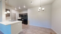This 1-bedroom, 1-bathroom unit at Silverleaf in Orange, Texas offers a well-designed single-floor layout that maximizes every square foot. The open-concept living and kitchen area serves as the heart of the home, anchored by a peninsula island with a built-in sink and white countertop, illuminated by pendant lighting overhead. The kitchen is equipped with dark espresso cabinetry, black appliances including a refrigerator, range, and over-the-range microwave, and flows seamlessly into the dining and living areas. Light wood-style vinyl flooring extends throughout the unit, providing a clean and cohesive aesthetic. An elegant chandelier accents the dining area, adding a touch of warmth to the open space. The bedroom is a comfortable size, featuring a ceiling fan, a large window with blinds that allows natural light to fill the room, and easy access to the closet. The bathroom includes a dark-cabinetry vanity with a white countertop, a large mirror with an illuminated vanity light bar, and wood-style flooring consistent with the rest of the unit. Additional spaces include a utility room and hallway, contributing to the overall functional flow of this thoughtfully laid-out home.