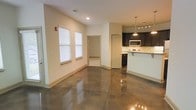 Located at 531 Old Maccumber Station Rd in Wilmington, North Carolina, this single-floor space offers a clean, modern aesthetic anchored by striking polished concrete floors that reflect light throughout the open layout. The main living area is bright and airy, with natural light streaming in through multiple windows dressed with white blinds, complementing the neutral, cream-toned walls and white baseboards that give the space a crisp, well-maintained appearance.

The open-concept design flows seamlessly into the kitchen, which is outfitted with dark espresso cabinetry, light stone countertops, and stainless steel appliances including a microwave and range. A breakfast bar extends from the counter, providing a casual dining or workspace option. Overhead, pendant lighting and a track light fixture illuminate the kitchen area with a modern touch.

Adjacent to the main living space, a doorway leads to an additional room or storage area, adding functional utility to the layout. The space also features recessed ceiling lights and visible HVAC vents, ensuring comfort throughout. Overall, the unit presents a contemporary, low-maintenance environment well-suited for a variety of uses, combining industrial-inspired flooring with modern finishes for a cohesive and inviting atmosphere.