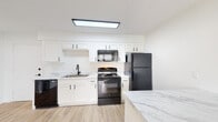 Located at 700 Morreene Rd in Durham, North Carolina, this single-floor unit offers a clean, modern aesthetic throughout. The open-concept kitchen and living area serves as the heart of the home, featuring light wood-style flooring that extends across the main living spaces. The kitchen is well-appointed with crisp white shaker cabinetry with black hardware, marble-look countertops, and a suite of black GE appliances including an electric range, over-the-range microwave, refrigerator, and dishwasher. A center island provides additional counter space and a natural division between the kitchen and the open living area. Natural light filters in through windows fitted with horizontal blinds. The bedrooms offer a comfortable contrast with plush carpeting underfoot, and each room includes closet storage with built-in shelving. One bedroom features light wood-style flooring and an open shelving unit, providing additional flexibility. The bathroom is finished in clean white tones, complete with a full tub-shower combination. Throughout the unit, a neutral white color palette and consistent use of black hardware accents create a cohesive, contemporary feel.