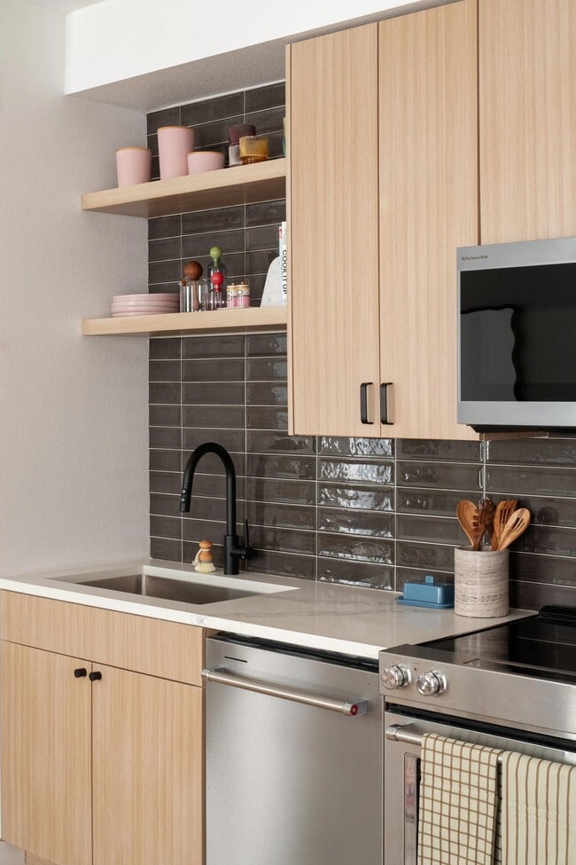 Streamlined cabinetry, open shelving, and a glossy tile backsplash bring warmth and texture to this thoughtfully designed kitchen. - Modera Rio Salado