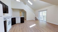 Located at 31 Harbor Dr in Claymont, Delaware, this two-story residence offers a thoughtfully designed open-concept layout filled with natural light. The main level immediately impresses with dramatically vaulted ceilings that soar overhead, enhanced by skylights that flood the interior with bright, natural illumination. Light wood-tone flooring runs throughout, complementing the clean, neutral wall palette and creating a warm, airy atmosphere.

The kitchen is positioned as a central feature of the main level, showcasing dark espresso cabinetry paired with light granite countertops and white appliances, including a dishwasher. It opens seamlessly into the living area, making the space ideal for both everyday living and entertaining. A staircase with a clean, white finish rises gracefully from the main floor to the upper level, adding a striking architectural element to the space.

At the rear of the main level, a sliding glass door leads to a private balcony, offering pleasant outdoor views and allowing additional natural light to pour into the living area. The upper floor provides additional living space, accessible via the interior staircase. Overall, the residence combines functional design with elevated architectural details, creating a bright and inviting home environment.