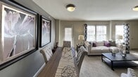 This single-floor residence offers a thoughtfully designed layout that balances comfort and functionality throughout its interconnected spaces. The open-concept living and dining area serves as the heart of the home, featuring neutral gray walls, plush carpeting, and multiple windows that allow generous natural light to fill the space. The living room accommodates a sectional sofa with accent pillows, a central coffee table, and bold wall art that adds a pop of color to the understated palette.

The kitchen is well-equipped with white shaker-style cabinetry, dark granite-look countertops, stainless steel appliances including a gas range, over-the-range microwave, and a French door refrigerator. A peninsula with a built-in sink provides additional workspace and casual seating potential, while wood-look tile flooring grounds the space with a warm, durable finish.

The bedroom features soft carpeting, a ceiling fan with integrated lighting, and a window dressed in light curtains that invite natural brightness. Dark wood furnishings provide an appealing contrast to the room's neutral tones.

The bathroom is finished with a dark granite vanity top, white cabinetry, wood-look tile flooring, and a tiled shower-tub combination, creating a clean and modern aesthetic that connects directly to the adjacent bedroom.