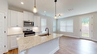Located in Suwanee, GA, this well-appointed two-story home offers a clean, modern aesthetic throughout. The heart of the home is a bright, open-concept kitchen featuring crisp white shaker cabinetry, a classic subway tile backsplash, and a generous central island topped with light granite countertops. A matte black undermount sink and coordinating pendant lights add a stylish contrast to the white finishes. Stainless steel appliances, including a gas range, over-the-range microwave, and a French door refrigerator, complete the chef-ready space. The kitchen flows naturally into a dining and living area bathed in natural light from multiple windows with white blinds and a glass-panel exterior door that leads outdoors. Hardwood-style flooring runs throughout the main level, lending warmth and continuity. Upstairs, carpeted bedrooms offer a comfortable retreat, each with ceiling fans and ample natural light. The bathrooms are finished with wood-toned flooring, white subway tile surrounds in the tub-shower, and white vanities with matte black hardware. A private water closet adds a practical touch. Neutral wall tones and clean architectural lines throughout create a fresh, move-in-ready atmosphere suited to a variety of lifestyles.