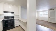 Located in Nashville's Midtown neighborhood, this two-bedroom, two-bathroom residence offers a practical and efficiently organized single-floor layout. The kitchen is thoughtfully designed with white cabinetry extending to the ceiling, black appliances including a refrigerator and range, a stainless microwave, and a light-toned countertop that extends outward as a pass-through bar — creating a natural connection to the adjacent living area. The flooring transitions from wood-look planks in the kitchen and hallway to plush, neutral-toned carpet throughout the living and bedroom spaces. Both bedrooms are well-proportioned, featuring built-in closets with shelving and windows fitted with horizontal blinds that allow natural light while maintaining privacy. The primary bedroom is notably spacious with a bright, open feel. The two bathrooms are clean and functional: one features a tiled tub-shower combination with blue-gray tile surround, while the other offers a classic white-tiled tub-shower, each with a vanity, mirror, and wood-look flooring. A connecting hallway ties all rooms together efficiently. Textured ceilings and neutral white walls throughout give the space a bright, move-in-ready appearance.