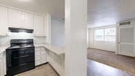 Located in Nashville's Midtown neighborhood, this two-bedroom, two-bathroom residence offers a practical and efficiently organized single-floor layout. The kitchen is thoughtfully designed with white cabinetry extending to the ceiling, black appliances including a refrigerator and range, a stainless microwave, and a light-toned countertop that extends outward as a pass-through bar — creating a natural connection to the adjacent living area. The flooring transitions from wood-look planks in the kitchen and hallway to plush, neutral-toned carpet throughout the living and bedroom spaces. Both bedrooms are well-proportioned, featuring built-in closets with shelving and windows fitted with horizontal blinds that allow natural light while maintaining privacy. The primary bedroom is notably spacious with a bright, open feel. The two bathrooms are clean and functional: one features a tiled tub-shower combination with blue-gray tile surround, while the other offers a classic white-tiled tub-shower, each with a vanity, mirror, and wood-look flooring. A connecting hallway ties all rooms together efficiently. Textured ceilings and neutral white walls throughout give the space a bright, move-in-ready appearance.