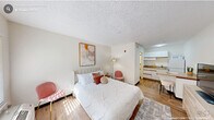 Located at Ivy Creek Blvd in Durham, NC, this compact, single-floor studio unit offers a thoughtfully designed open-concept layout that maximizes every inch of available space. The main living and sleeping area features warm wood-tone flooring, crisp white walls, and a textured ceiling, creating a clean and welcoming atmosphere. Natural light filters in through a window with blinds near the front entry door, brightening the space throughout the day. A built-in open closet with wire shelving provides convenient storage directly within the main room, complemented by additional dresser storage. The compact kitchen is efficiently arranged with white cabinetry, a countertop with bar seating, and essential appliances including a refrigerator and stovetop — neatly tucked adjacent to the main living area. The bathroom continues the unit's consistent wood-tone flooring and features a vanity with countertop storage, keeping the design cohesive. A wall-mounted HVAC unit ensures year-round climate control. The overall design is straightforward and functional, making this unit well-suited for a single occupant seeking a low-maintenance, self-contained living space in Durham, North Carolina.