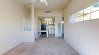 Located at 900 Country Club Dr SE in Rio Rancho, New Mexico, this single-floor unit offers a practical and well-organized layout designed to maximize its compact footprint. The combined kitchen and living area forms the heart of the space, featuring an open design that promotes a sense of connectivity. The kitchen is equipped with a black range, a black refrigerator, a double-basin sink, and a mix of white cabinetry with wood-toned accents. A light-colored countertop peninsula provides additional workspace and doubles as a casual dining surface. Wood-look flooring runs through the kitchen, transitioning to plush carpet in the living area, which is topped with a ceiling fan and benefits from natural light through windows positioned high on the walls. A hallway connects the living space to the two bathrooms, one of which features a full tub/shower combo with a window for natural light. Storage is well addressed throughout, with three closets — including a walk-in closet outfitted with built-in shelving and hanging rods. The neutral, warm-toned walls throughout create a clean and inviting ambiance, making the space feel open and easy to personalize.